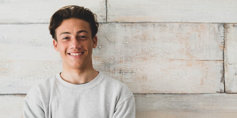 jeune homme aux cheveux bruns devant un mur clair